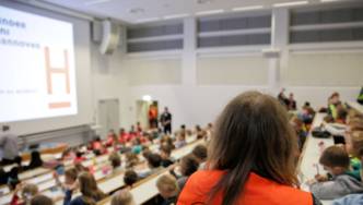 Gefüllter Hörsaal, im Vordergrund eine Frau mit einer roten Weste mit dem Aufdruck Kinder Uni Hannover