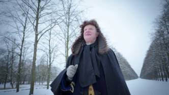 Mann mit historischer Perücke in verschneiter Allee.